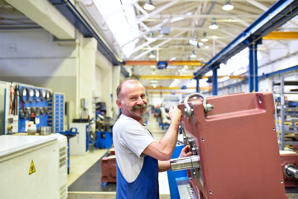 A smiling maintenance worker in blue overalls maintaining a MITRPAK right angle gearbox in a manufacturing warehouse