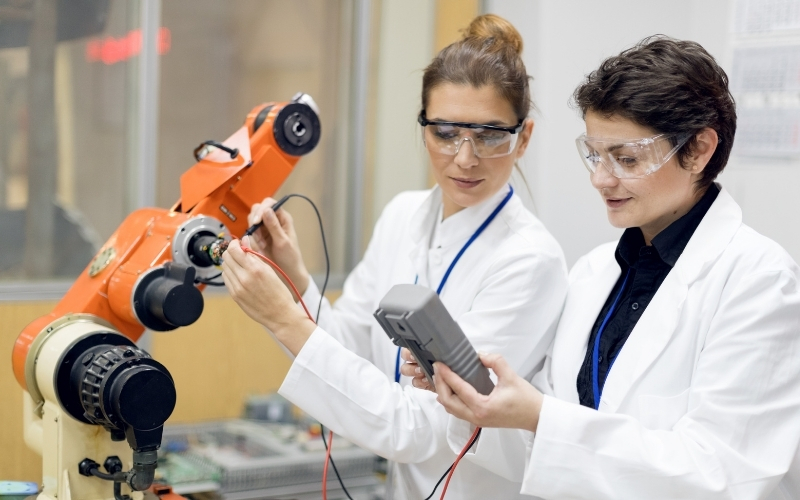 Two engineers testing right angle drive actuation in an orange robotic arm.