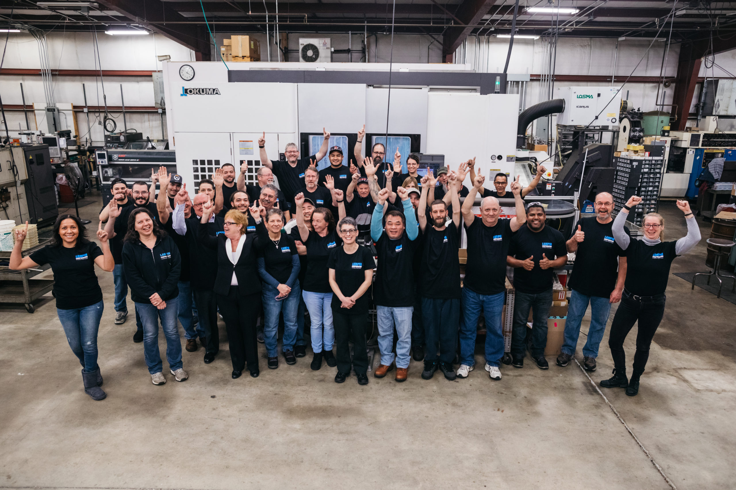 Lampin's employee owners are gathered in front of a machine with their hands raised in the air to express joy.