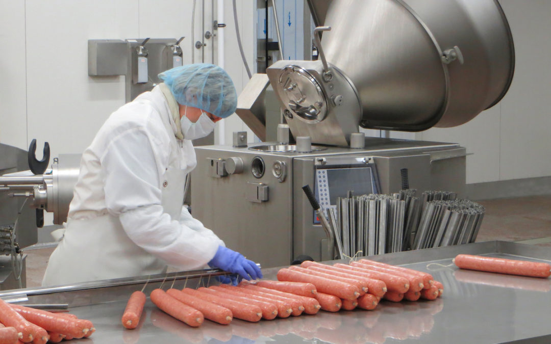 Butcher processing sausages at meat factory.