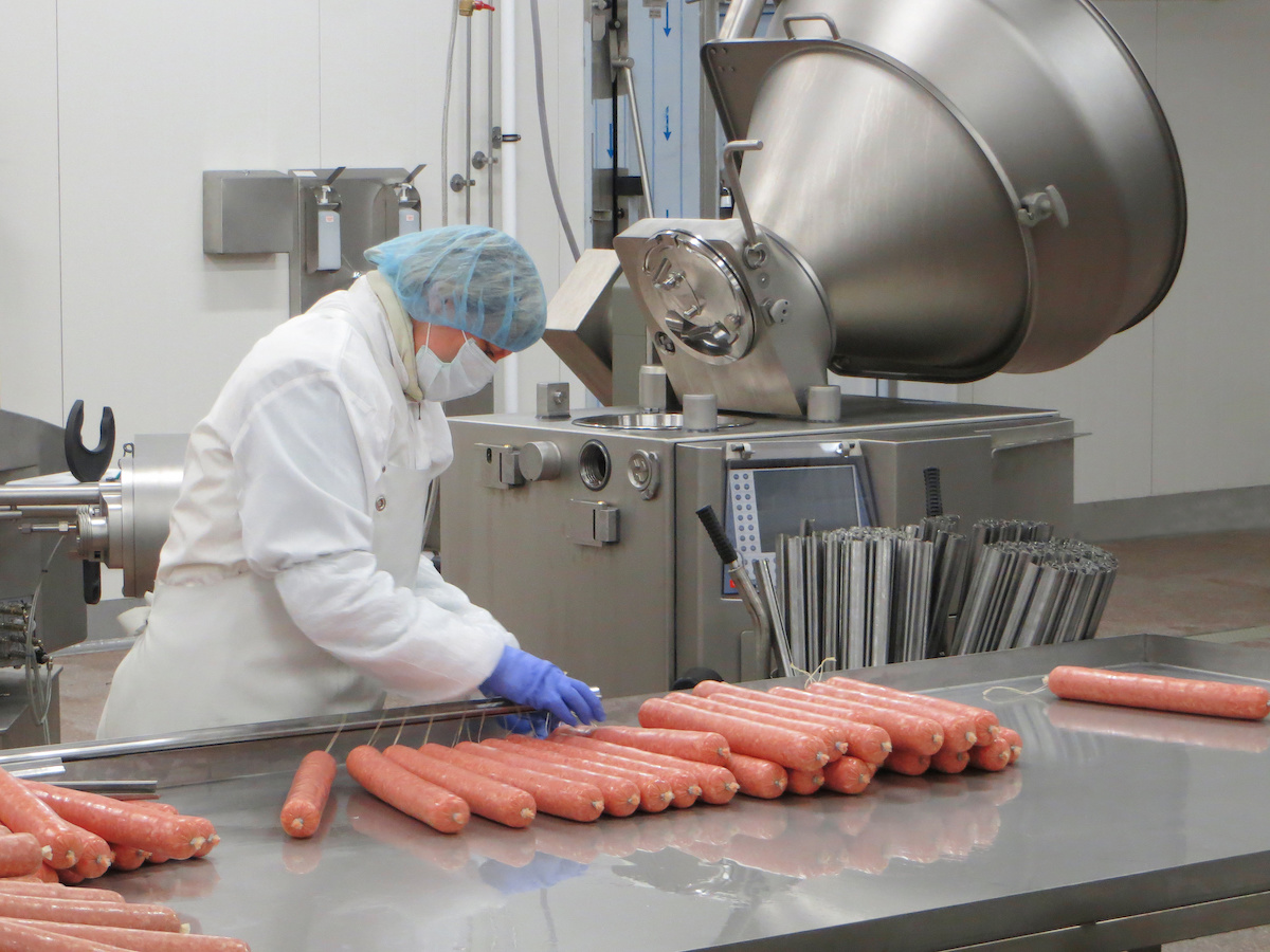 Butcher processing sausages at meat factory.