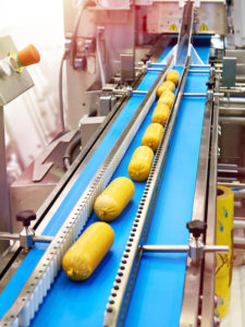 Sausages in yellow plastic chub packaging on a blue conveyor belt at a food processing factory.
