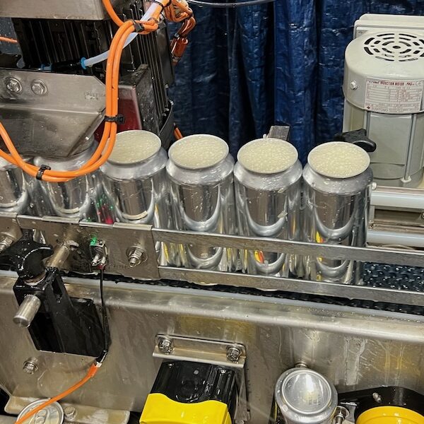 The canning line; four filled, unlabeled cans travel down a belt.